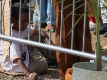 Criança sentada em papelão assiste a missa celebrada hoje (10) pelo papa Francisco em Timor-Leste. | Crédito: Daniel Ibáñez/EWTN News