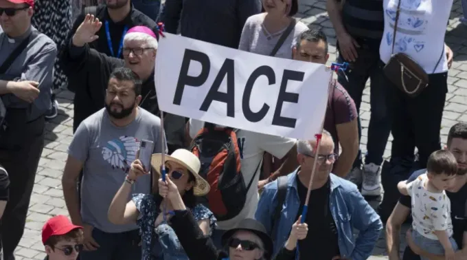 Peregrinos na praça de São Pedro com faixa que diz 