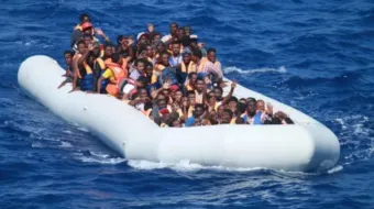 Migrantes a bordo de barco inflável no mar Mediterrâneo aproximam-se de um navio de guerra dos EUA.