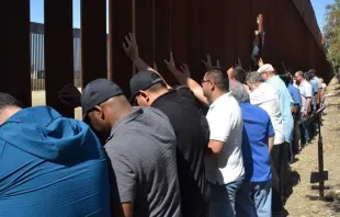 Sacerdotes scalabrinianos rezam diante do muro que separa México e Estados Unidos. Crédito: Cortesia Casa do Migrante em Tijuana.